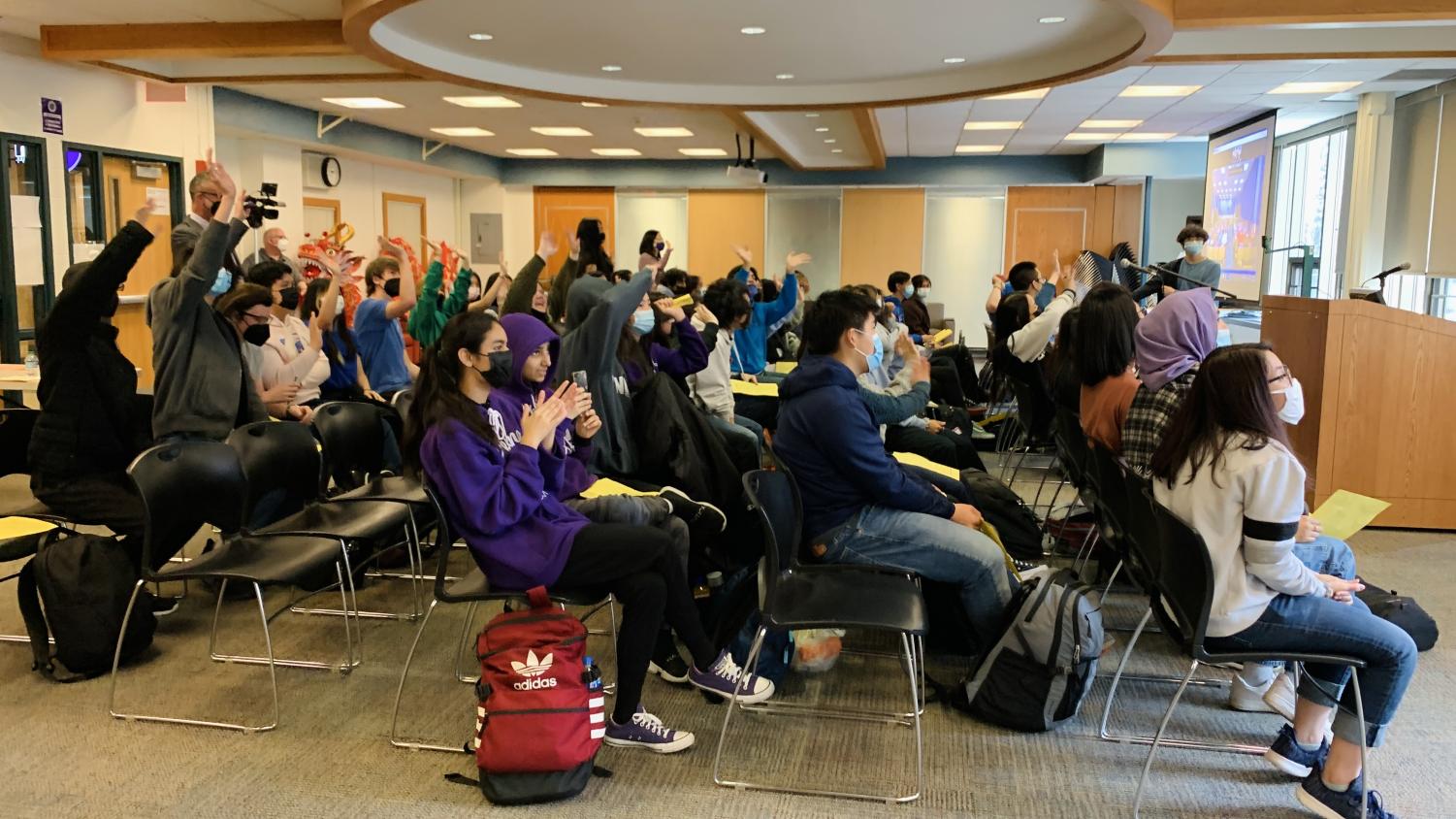 Chinese students gather in the New Commons and wave to the camera.